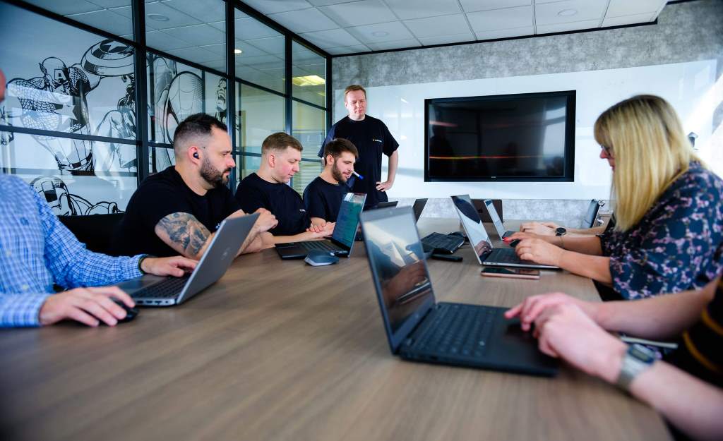 A small startup team reviews cybersecurity policies on a laptop in a modern office